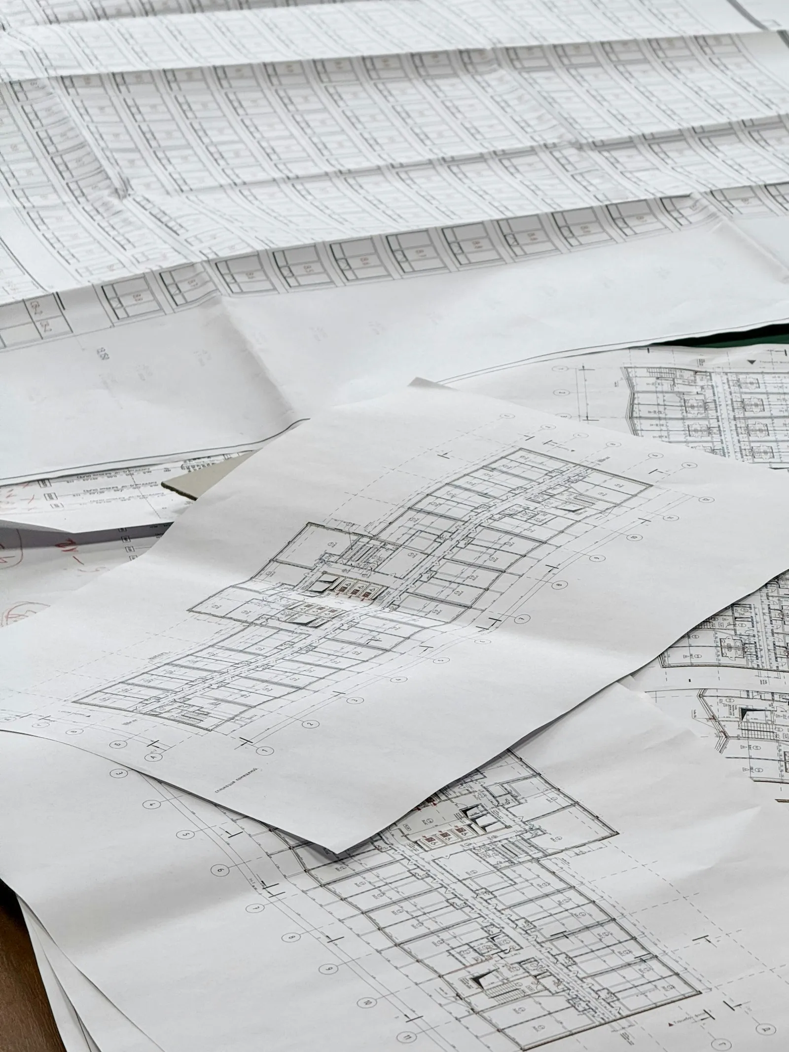 Tumpukan gambar denah dan blueprint arsitektur di atas meja kerja